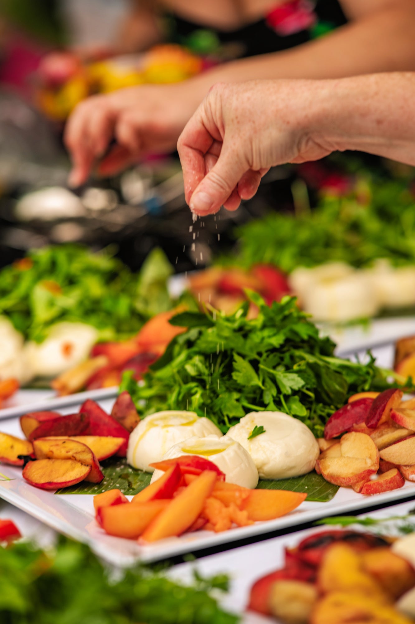 Chef preparing a fresh farm-to-table catering display with seasonal fruits, greens and artisan cheeses for a Shef Madres event.